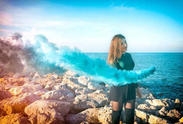 Foto mujer joven de pie junto al mar con llamarada de angustia contra el cielo despejado