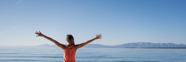 Mujer joven de pie junto al mar de la mañana saludando el nuevo día