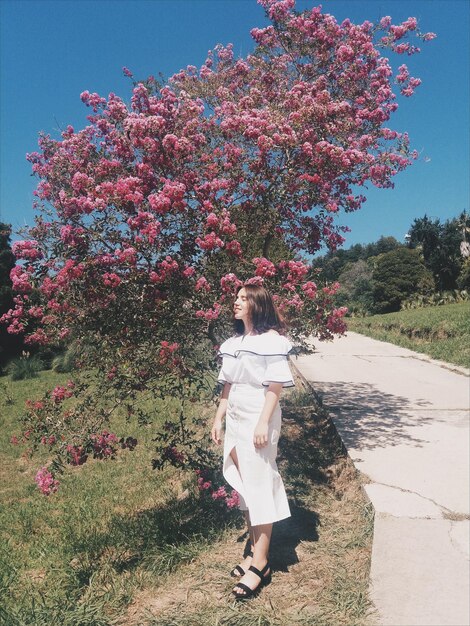 Foto mujer joven de pie junto a un árbol en flor