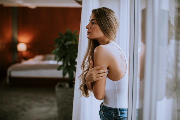 Mujer joven de pie junto a la ventana de la habitación