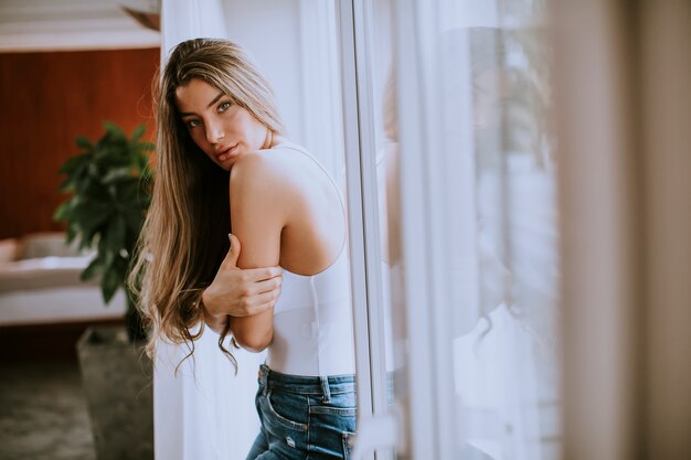 Mujer joven de pie junto a la ventana de la habitación