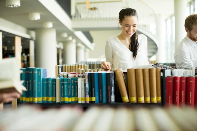 Mujer joven de pie y leyendo en la biblioteca