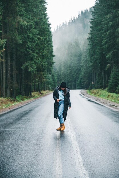 Mujer joven de pie en medio de la carretera en el bosque de montañas de invierno