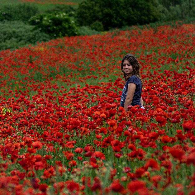 Foto mujer joven de pie en medio de las flores de amapola