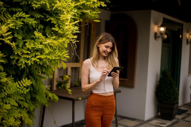 Mujer joven de pie en el patio trasero y a través de teléfono móvil