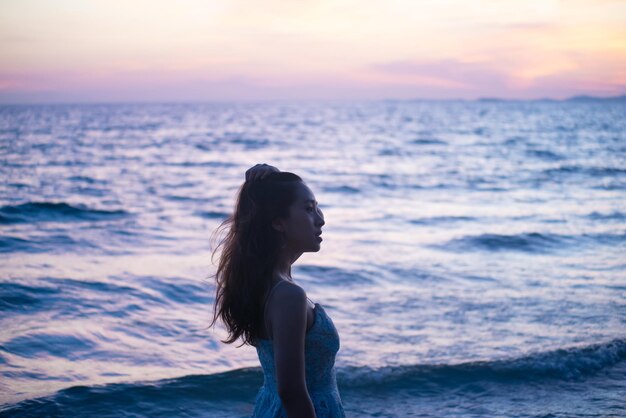 Foto mujer joven de pie en la playa durante la puesta de sol