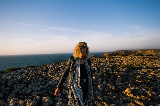 Foto mujer joven de pie en la roca junto al mar contra el cielo durante la puesta de sol