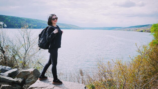 Mujer joven de pie en la roca por el mar contra el cielo