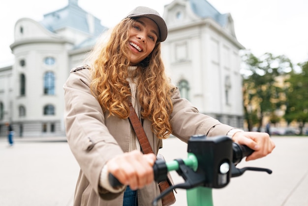 Mujer joven de pie en scooter eléctrico en la ciudad