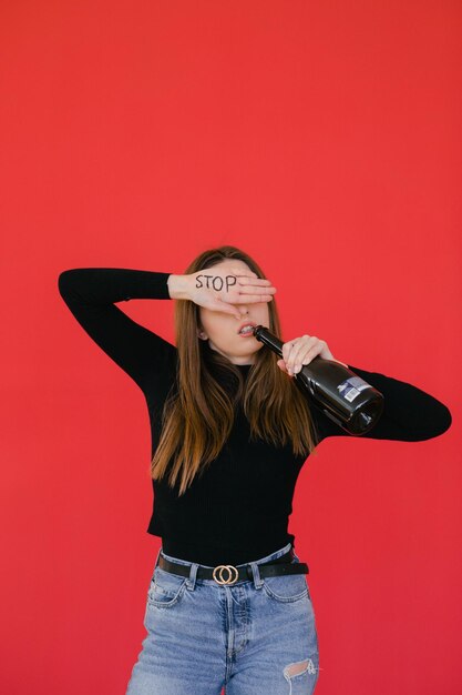 mujer joven de pie sobre fondo rojo y sosteniendo una botella de vino