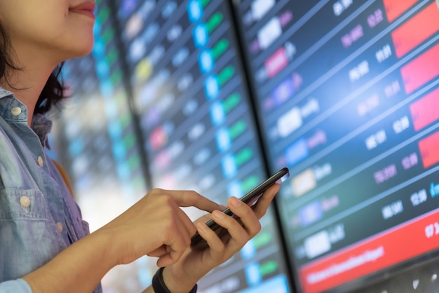 Foto mujer joven de pie sobre el tablero de información de vuelo mientras usa el teléfono inteligente.