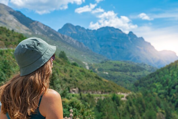 Mujer joven de pie solo al aire libre con montañas de bosque salvaje en segundo plano.