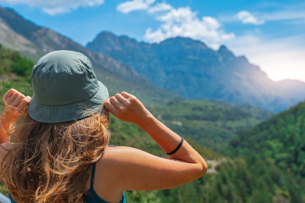 Mujer joven de pie solo al aire libre con montañas de bosque salvaje en segundo plano.