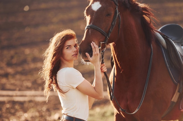 Mujer joven de pie con su caballo en el campo de la agricultura en el día soleado