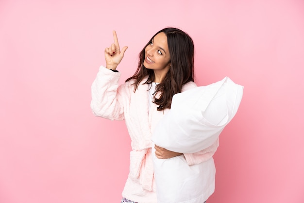 Mujer joven en pijama en pared rosa apuntando con el dedo índice una gran idea