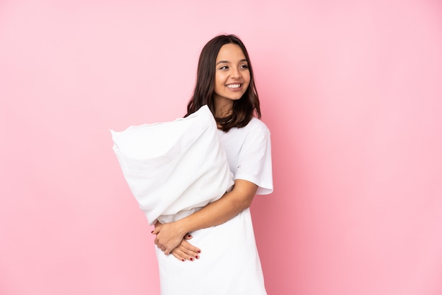 Mujer joven en pijama en pared rosa con los brazos cruzados y feliz