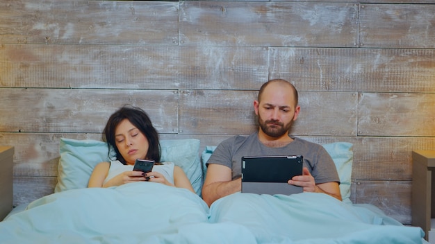 Mujer joven en pijama para quedarse dormido mientras su marido está usando la tableta.