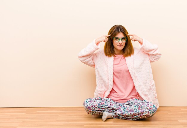 Mujer joven con pijama sentada en su casa con una mirada seria y concentrada, lluvia de ideas y pensando en un problema desafiante