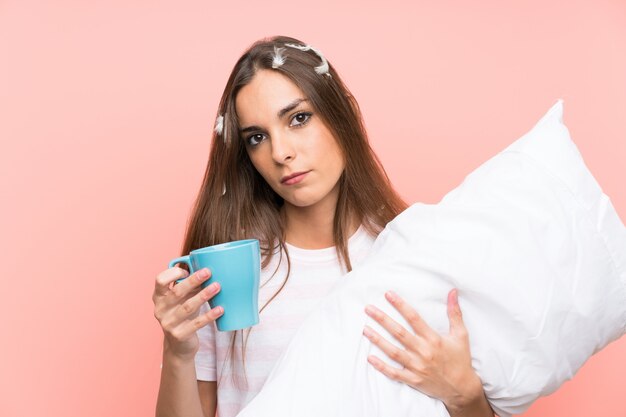 Mujer joven en pijama sobre fondo rosa aislado sosteniendo una taza de café