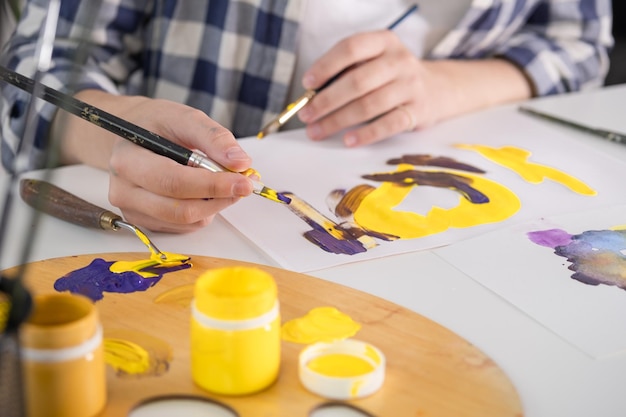 Una mujer joven pinta con gouache en casa Pasatiempos de dibujar con gouache Un ángulo cercano Pintura brillante y el proceso de dibujar con gouache