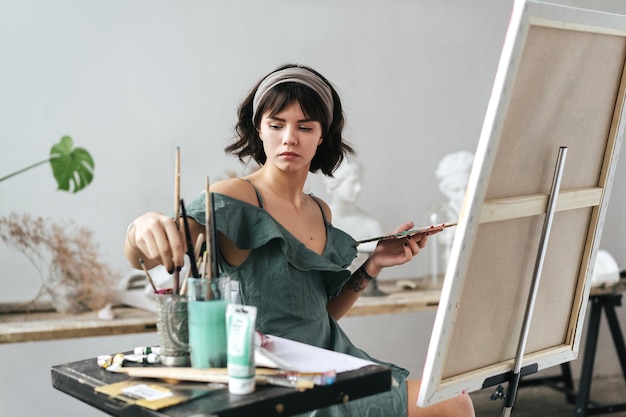 Foto mujer joven pintando en lienzo mientras está sentada en la mesa