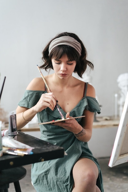 Foto mujer joven pintando en lienzo mientras está sentada en la mesa