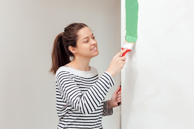 Mujer joven pintando la pared interior con pincel