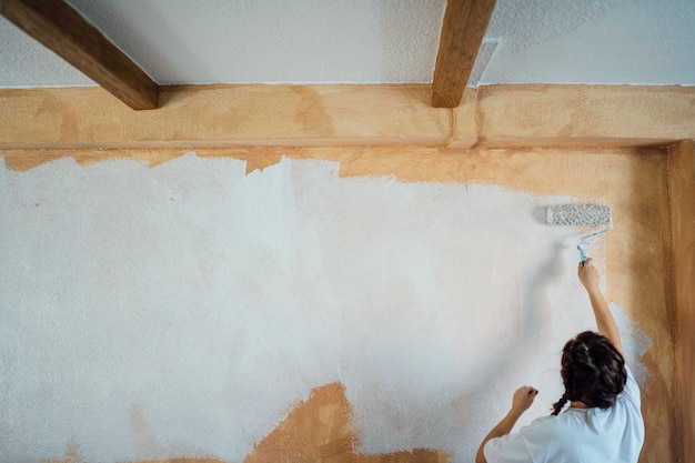 Mujer joven pintando las paredes de su casa.