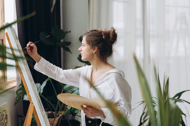 Mujer joven pintando con pincel sobre caballete