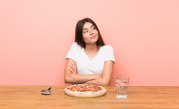 Foto mujer joven con una pizza haciendo dudas gesto mientras levanta los hombros