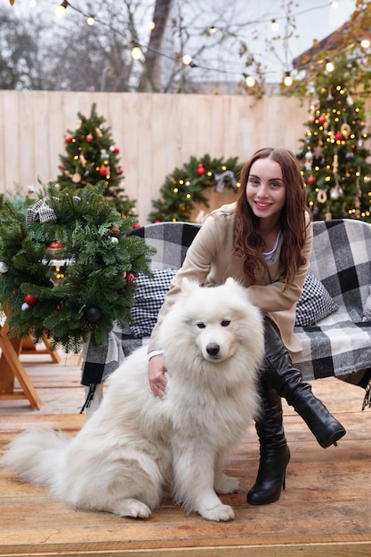 mujer joven, en, plano de fondo, de, árbol de navidad, con, blanco, samoyedo, perro, aire libre, patio, decoración, para, año nuevo