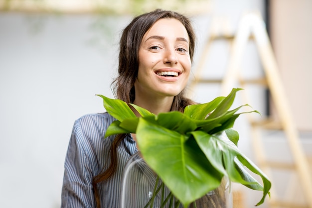 Mujer joven plantar casa con vegetación de pie con gran planta en la habitación