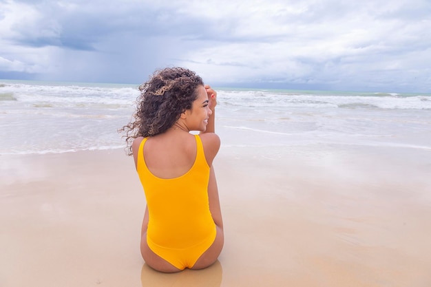 Mujer joven en la playa Mujer afro sentada en la arena de la playa en un hermoso día de verano