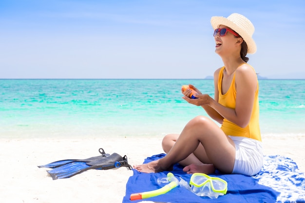 Mujer joven en la playa que aplica la crema de sol.