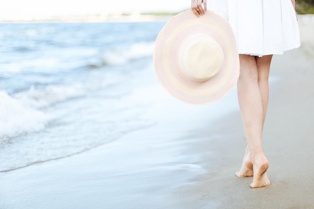 Mujer joven en una playa con un sombrero blanco. Piernas de cerca
