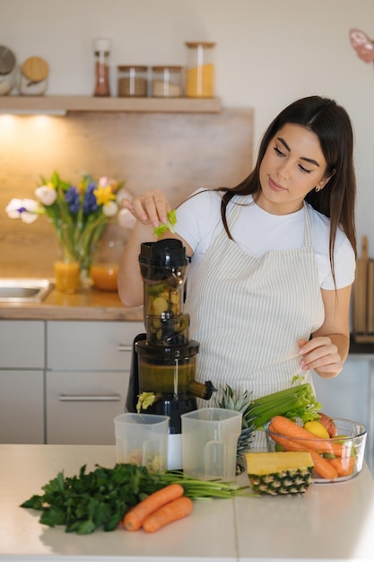 Mujer joven pone apio en el proceso de jugo de hacer bebida saludable