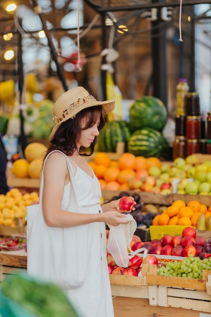 Mujer joven pone frutas y verduras en una bolsa de productos de algodón en el mercado de alimentos. Bolsa ecológica reutilizable para compras. Concepto de desperdicio cero.