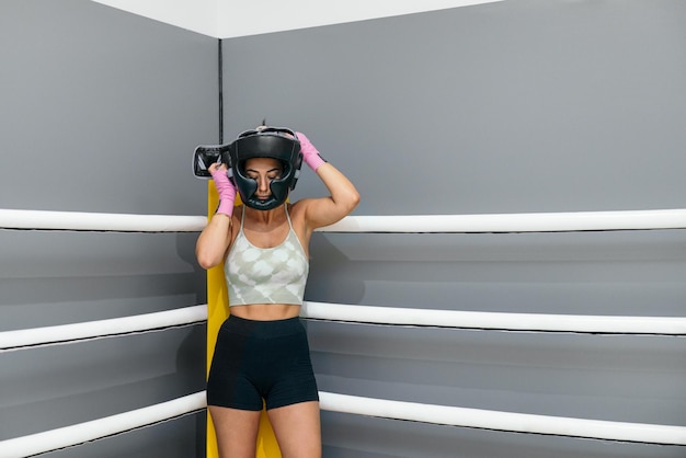 Mujer joven poniendo casco protector para practicar boxeo de pie en el ring de boxeo