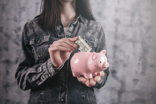 Mujer joven poniendo una moneda dentro de la hucha como ahorros para la inversión