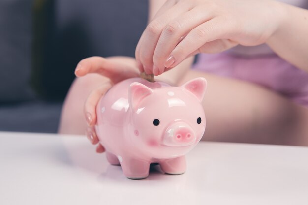 Mujer joven poniendo una moneda dentro de la hucha como ahorros para la inversión