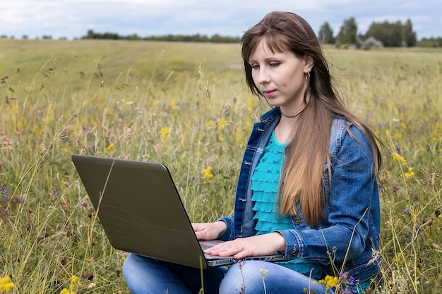 Mujer joven con portátil sentado sobre la hierba verde. chica con una computadora portátil en la naturaleza.