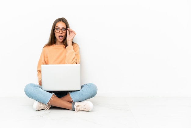 Mujer joven con un portátil sentado en el suelo con gafas y sorprendido