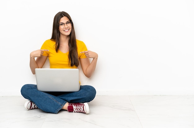 Mujer joven con un portátil sentado en el suelo orgulloso y satisfecho de sí mismo