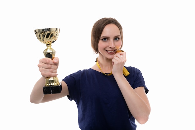 Una mujer joven posa con la copa del ganador y la medalla de oro sobre un fondo blanco.