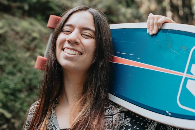 Mujer joven posando y sonriendo con una patinetaLongboarding en el bosque Actividades deportivas Gen Z