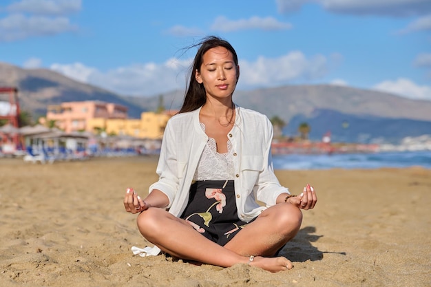 Mujer joven en posición de loto en la playa practicando yoga