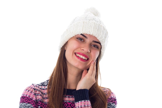 Mujer joven positiva con cabello largo con sombrero blanco y suéter morado sobre fondo blanco en el estudio