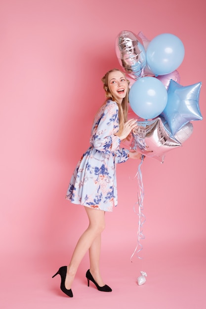 Mujer joven positiva con globos sobre una superficie rosa