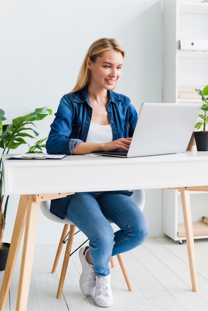 Foto mujer joven positiva que usa el ordenador portátil en lugar de trabajo