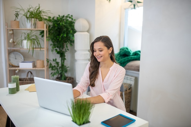 Mujer joven positiva trabajando en su computadora portátil mientras está sentado en la oficina